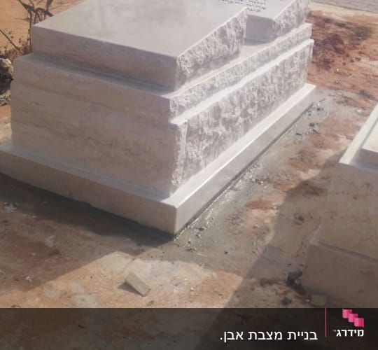 מצבת אבן בהירה במבנה מדורג עם שוליים מסותתים וכיתוב מוקפד